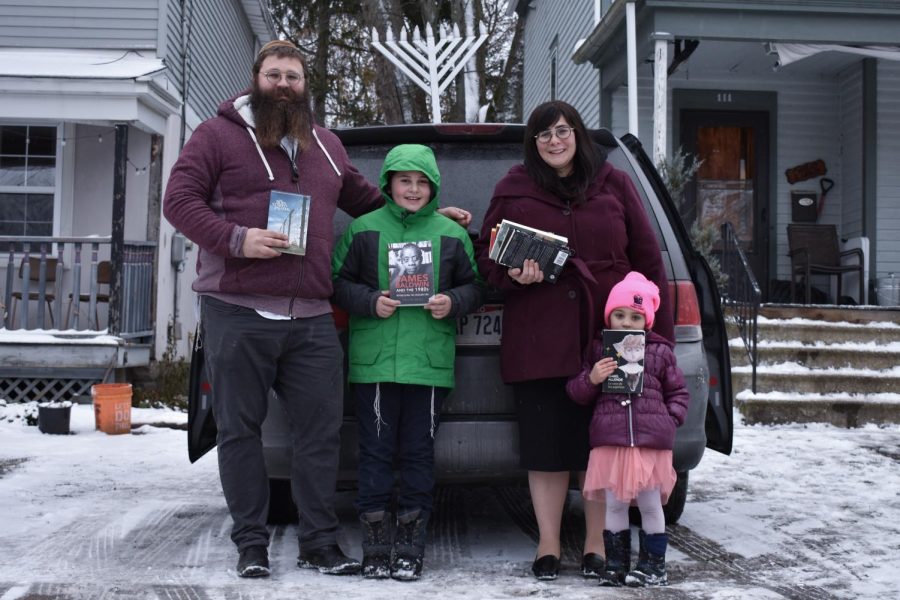 Rabbi Shlomo Elkan and wife Devorah Elkan standing in front of their home with two of their children holding books from the book drive.